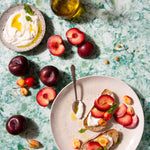A colorful green, blue, and white photo backdrop with a plate of food, fruits, and a bottle of oil arranged on it.