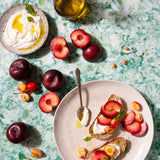 A colorful green, blue, and white photo backdrop with a plate of food, fruits, and a bottle of oil arranged on it.
