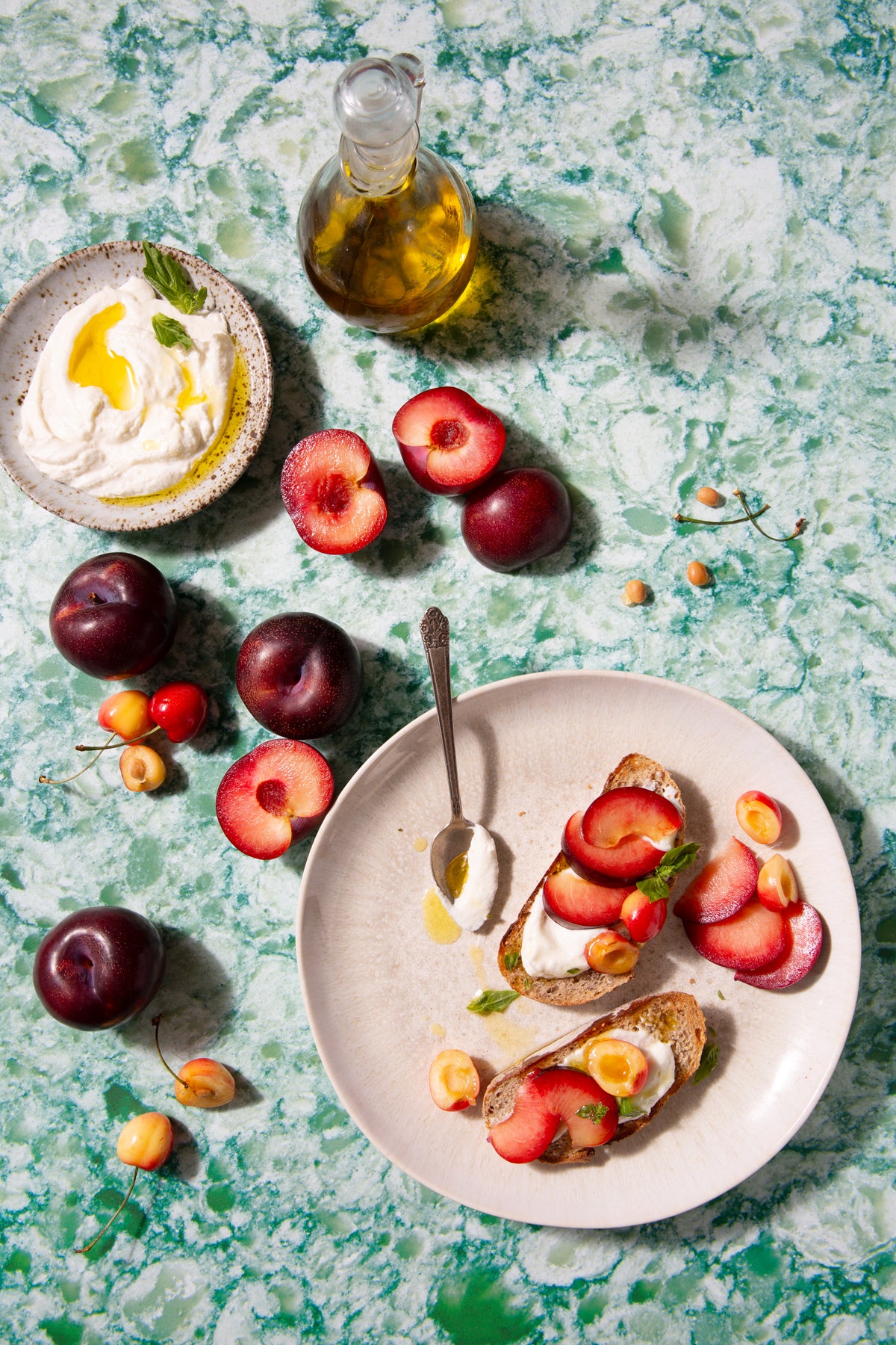 A colorful green, blue, and white photo backdrop with a plate of food, fruits, and a bottle of oil arranged on it.