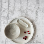 A gray, concrete texture photo backdrop is laid out flat, with a bowl and small red berries placed on it, indicating the backdrop's use for photography.