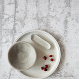 A gray, concrete texture photo backdrop is laid out flat, with a bowl and small red berries placed on it, indicating the backdrop's use for photography.