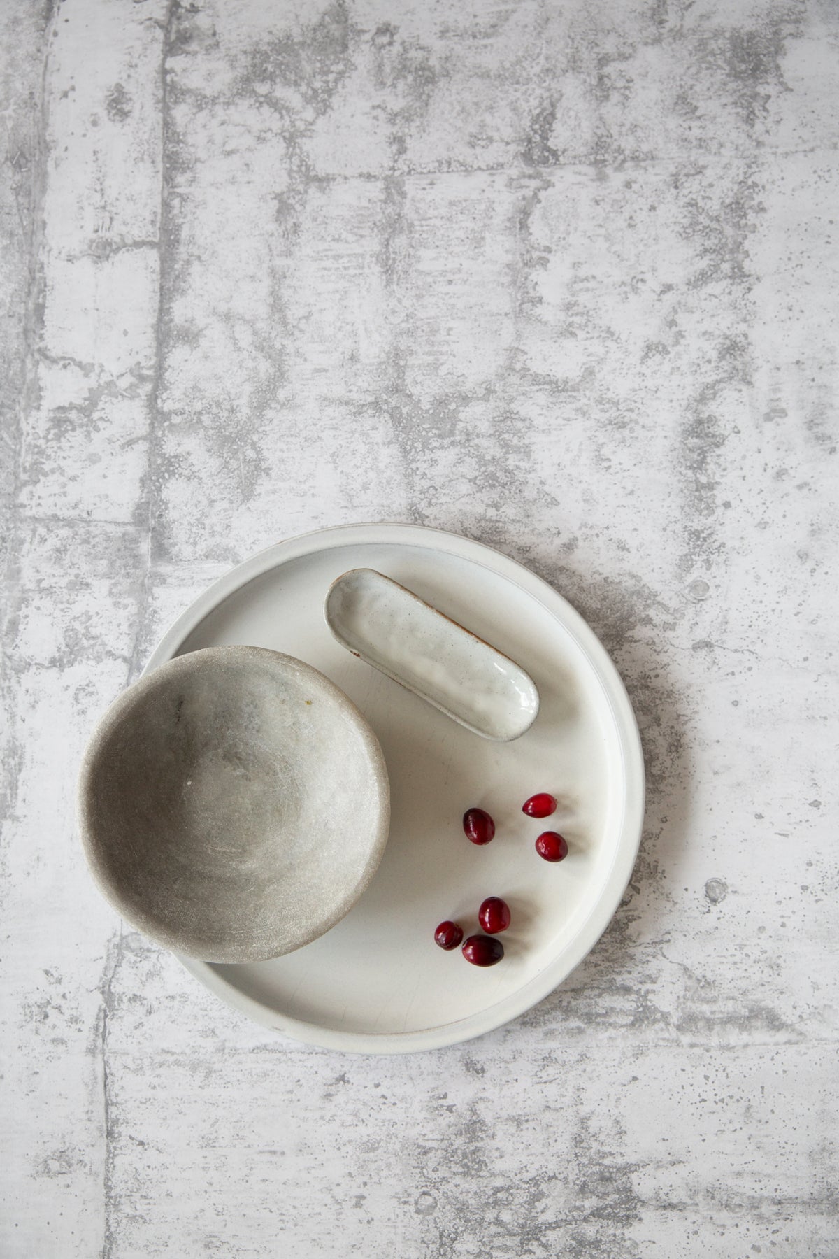 A gray, concrete texture photo backdrop is laid out flat, with a bowl and small red berries placed on it, indicating the backdrop's use for photography.