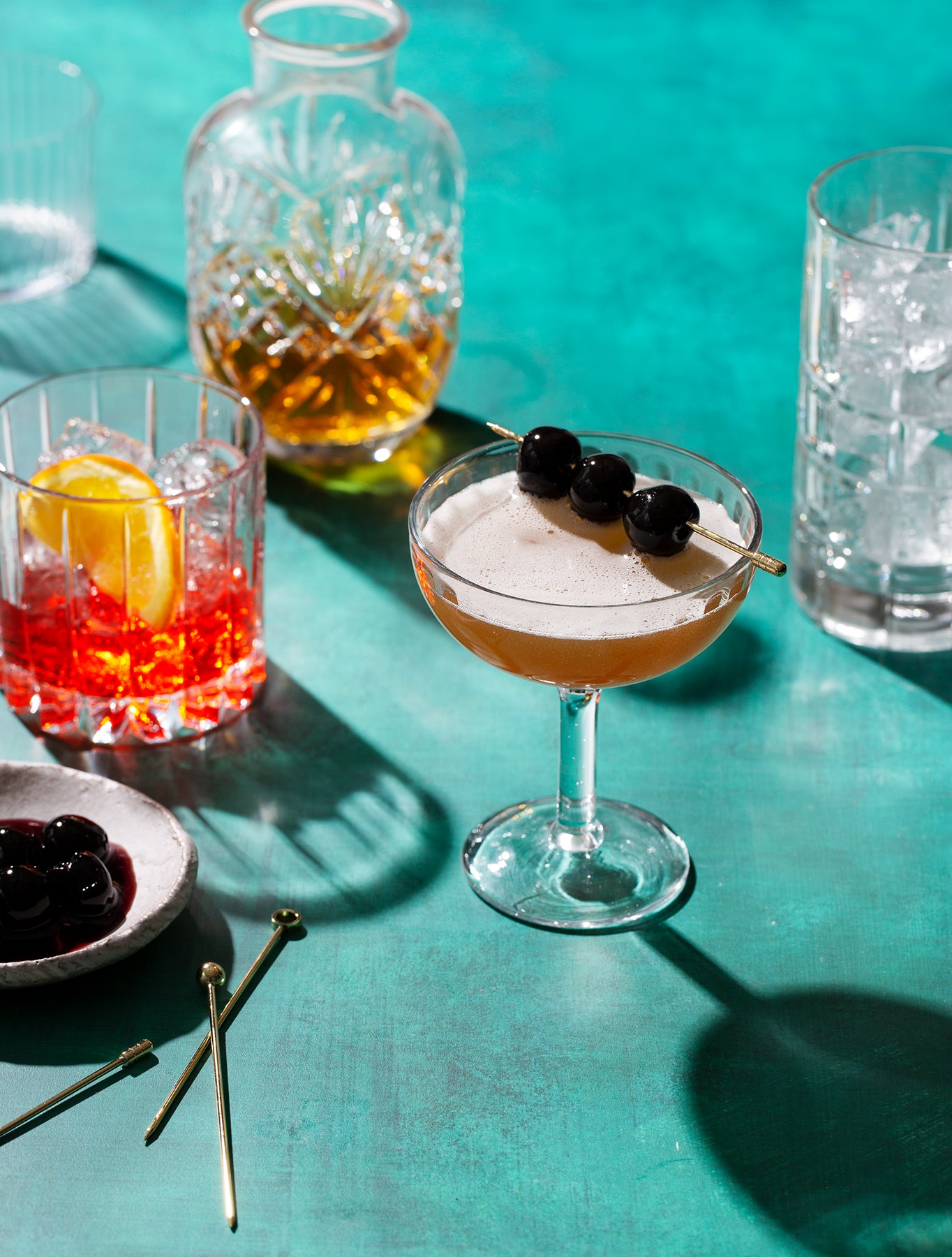 Cocktails on a turquoise photography backdrop with garnishes and glasses.