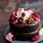 Dark metal photography surface with chocolate cake topped with fruit and flowers