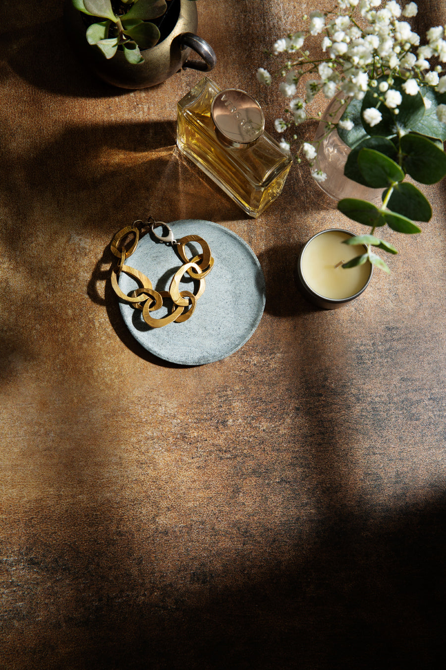 Dark and moody stone photography surface with perfume, jewelry and plants with dramatic shadows