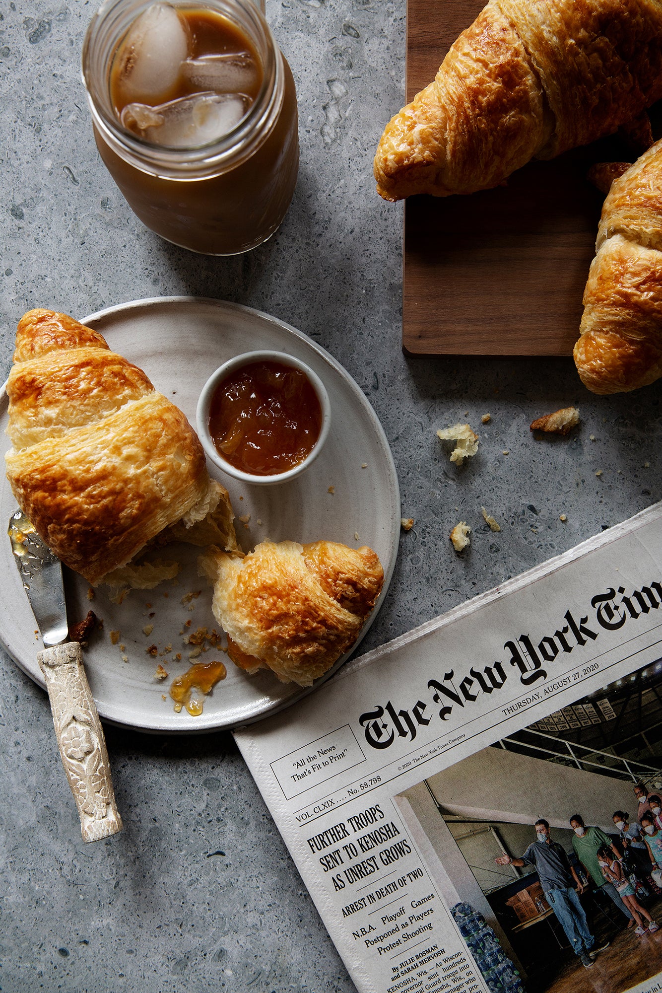 Rustic gray stone photography surface with croissants, iced coffee and newspaper