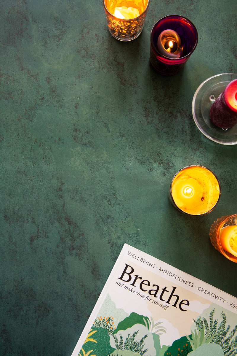 Dark green stone photography surface with candles and wellness magazine