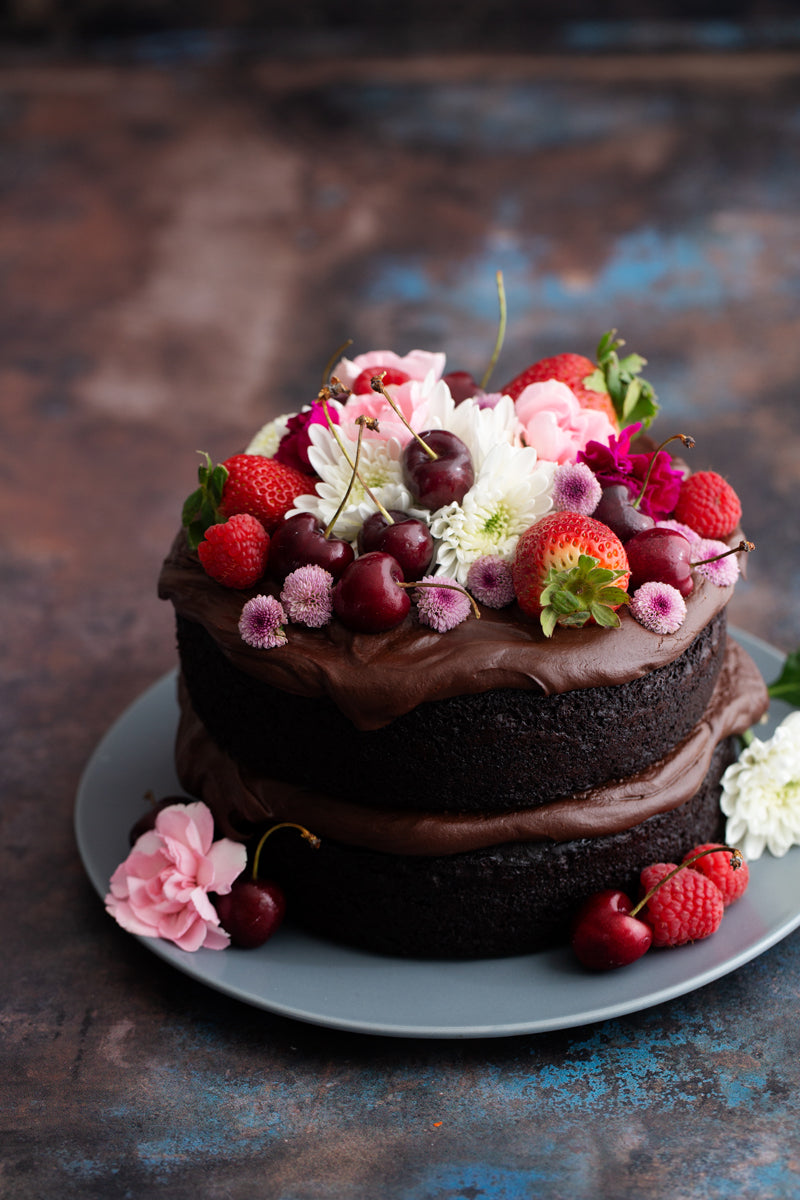 Dark metal photography surface with chocolate cake topped with fruit and flowers